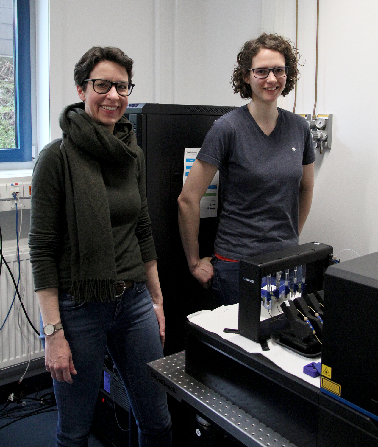 Sarah Köster (links) und Charlotta Lorenz (rechts) im Labor. Im Vordergrund ist die optische Falle zu sehen, an der die Experimente durchgeführt wurden.
