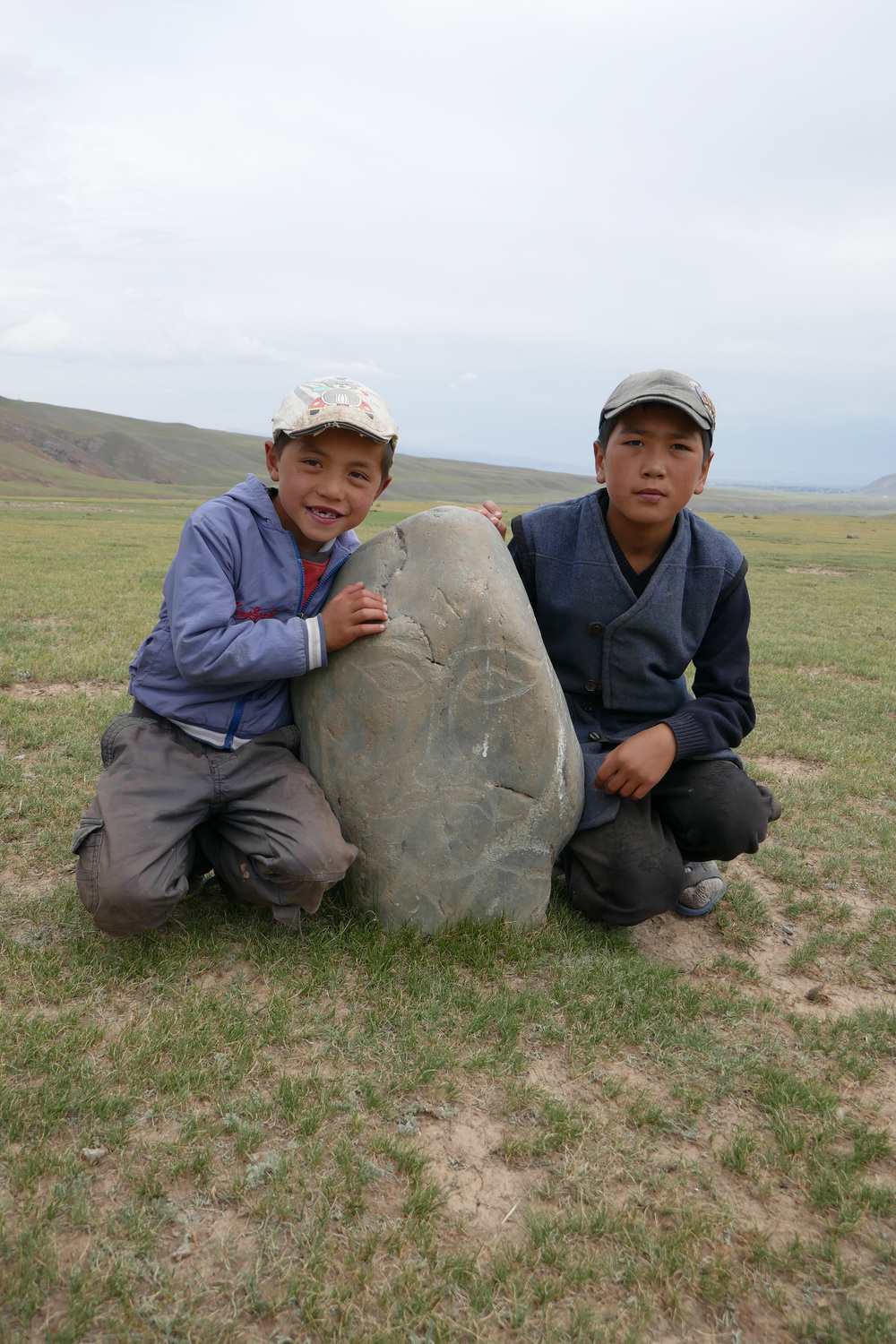 Zwei kirgisische Jungen zeigen einen Balbal, eine Steinfigur mit menschlichen Formen.